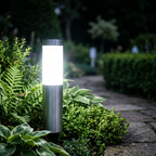 Close-up of a silver stainless steel solar path light glowing beside a UK garden path