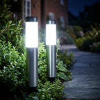 Close-up of two silver solar bollard lights glowing cool white beside a paved path