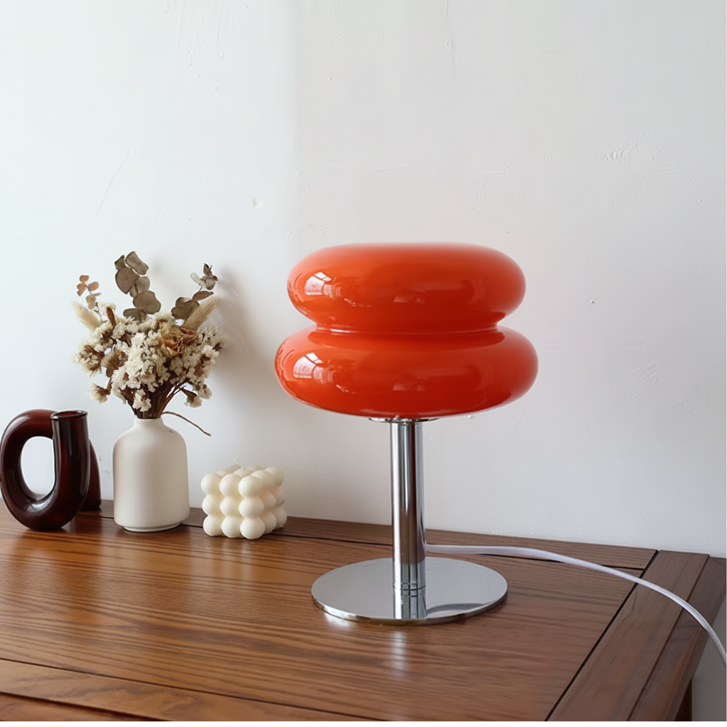 Orange macaron glass table lamp with a chrome base, on a wooden cabinet