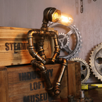 Square product image of the seated iron pipe robot lamp with warm illuminated bulb