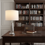 Vera crystal table lamp lit on a wooden desk in a home study, bookshelves behind